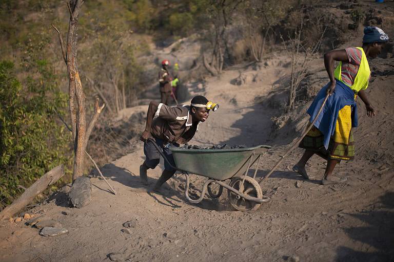 En mann triller en full trillebår opp en bakke utenfor en gruve i Malawi og en kvinne i Malawi